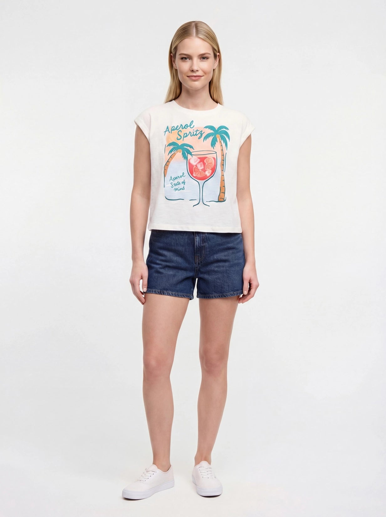 Front view of white t-shirt with "Aperol Spritz; Aperol State of Mind" text and graphic design featuring a cocktail and palm trees and jean shorts on a white background. 
