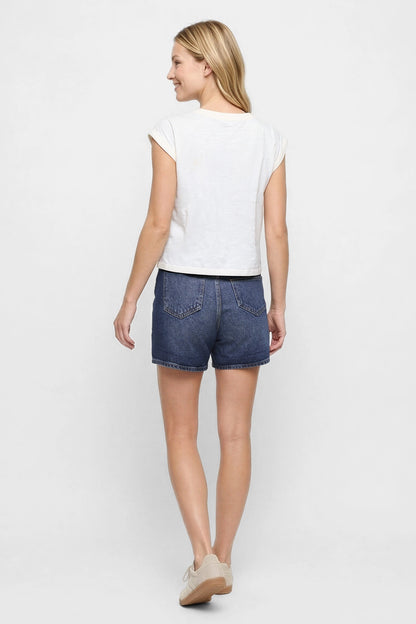 Back view of woman wearing a white cap sleeve tee and blue jeans shorts on a white background. 
