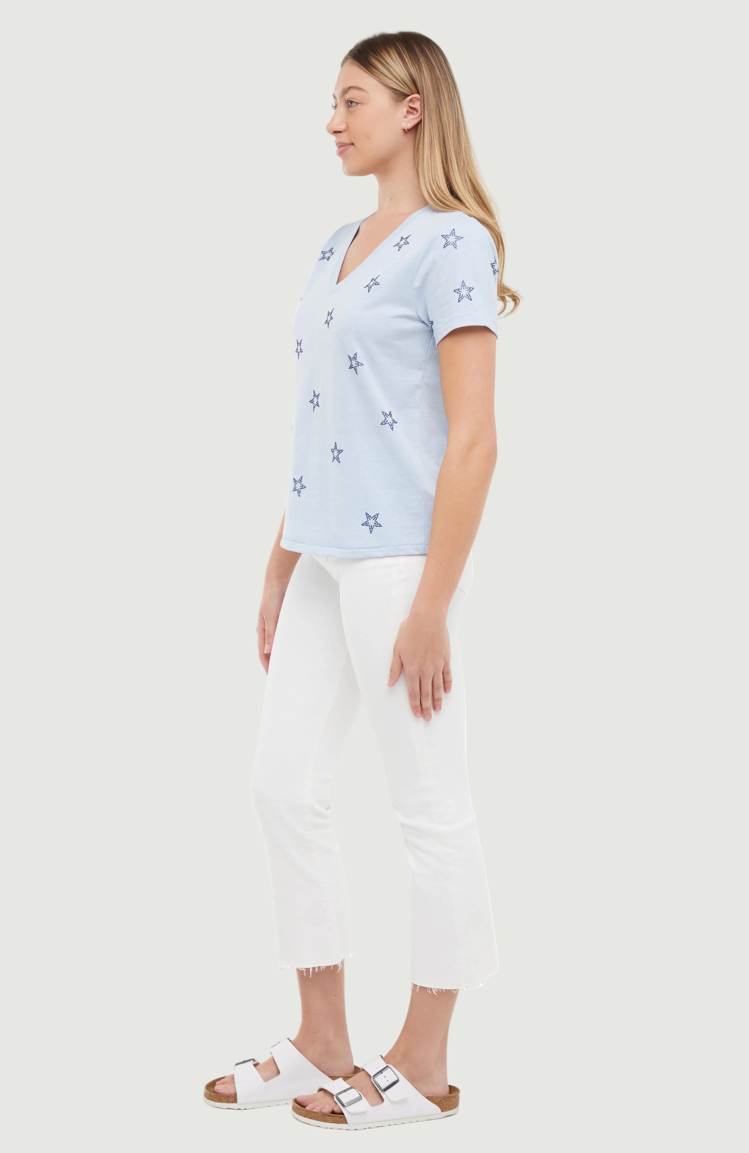 Side view of woman wearing a light blue t-shirt with blue rhinestone star patterns on a white background