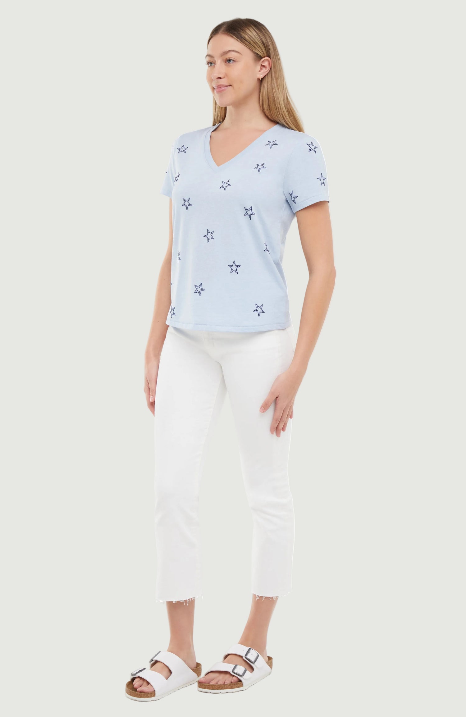 Side view of woman wearing a light blue t-shirt with blue rhinestone star patterns on a white background