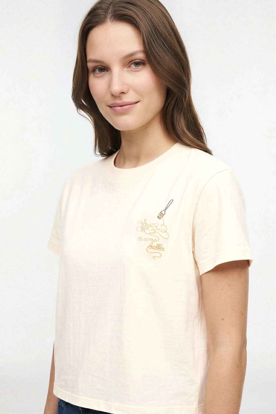 Close up view of woman wearing a pale yellow t-shirt with embroidered design of spaghetti and a fork, accompanied by the text &