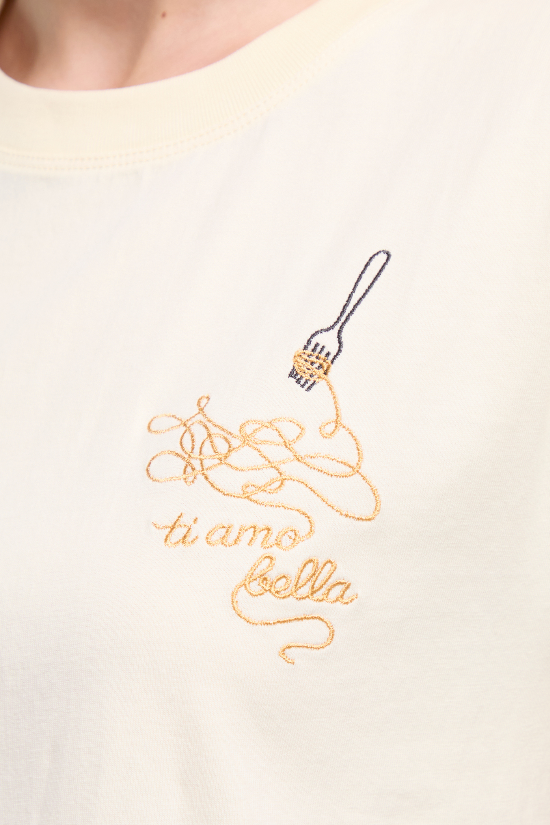 Close up view of t-shirt with embroidered design of spaghetti and a fork, accompanied by the text &