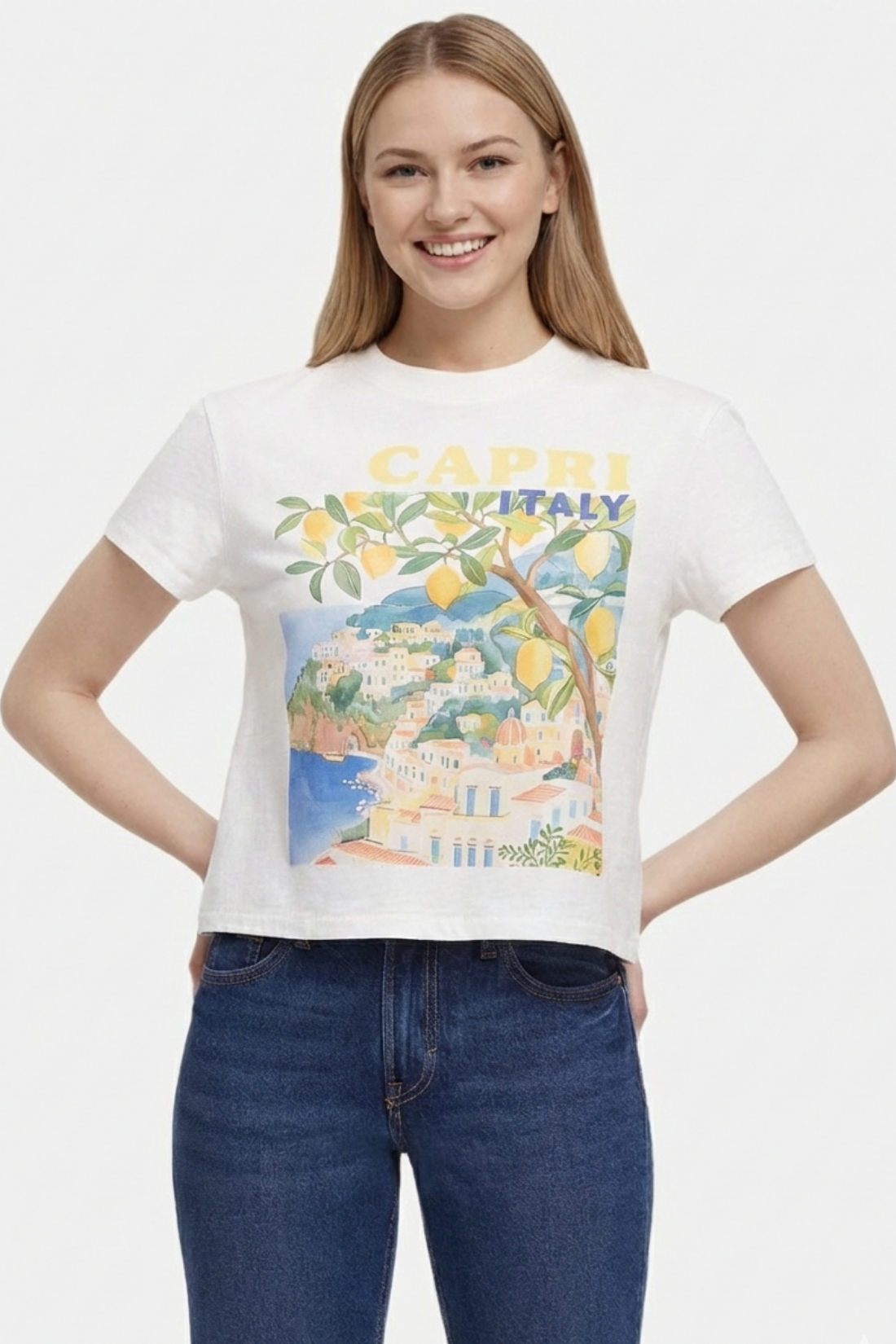 Woman wearing a white t-shirt with a colorful graphic design of Capri, Italy, featuring buildings, trees, and lemons and &