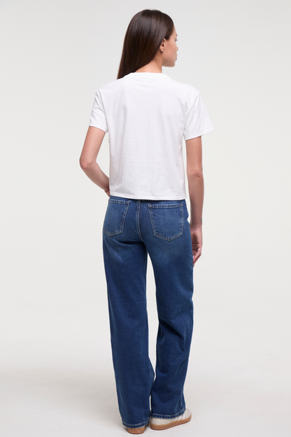 Back view of woman wearing a white t-shirt and blue jeans on a plain background. 