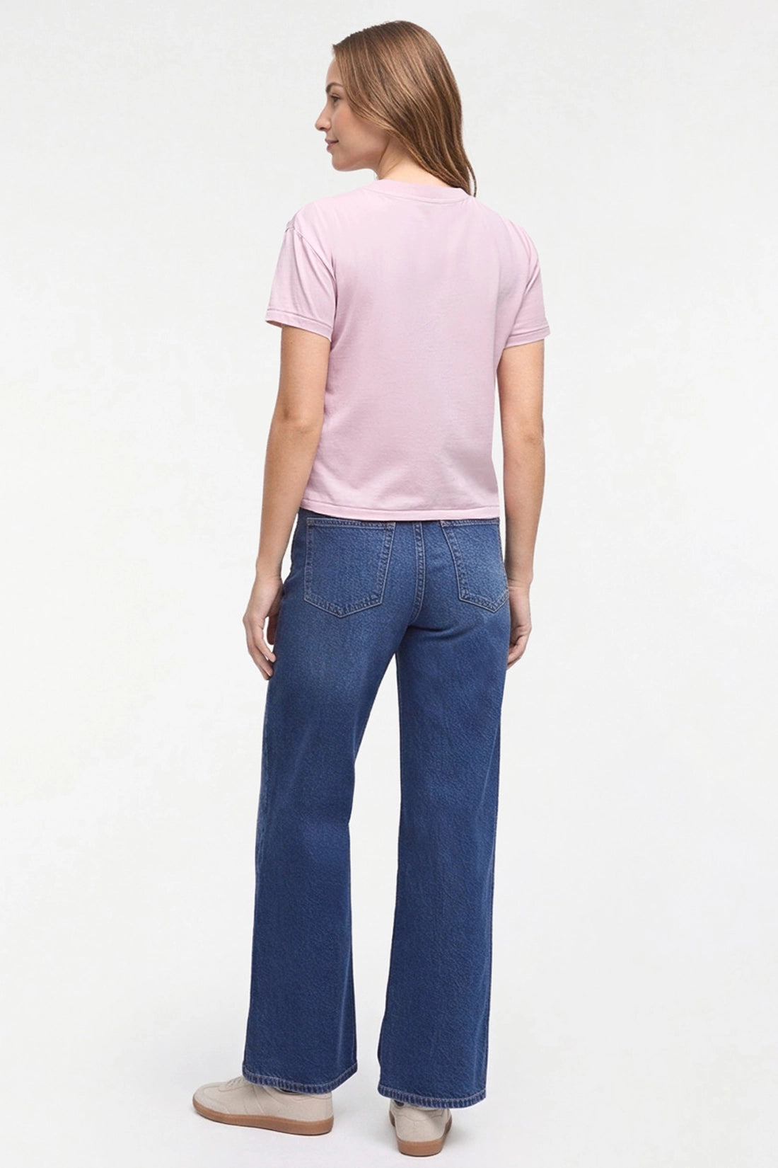 A woman shown from the back wearing a light pink short-sleeve t-shirt and dark blue wide-leg jeans, standing against a plain white studio background. 