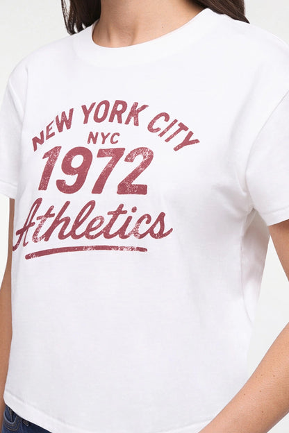 A close-up of a person wearing a white short-sleeve T-shirt with a distressed red graphic reading &