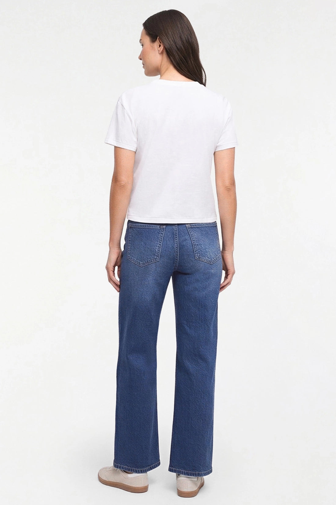A woman shown from the back wearing a white short-sleeve t-shirt and blue straight-leg jeans, standing against a plain white studio background. 