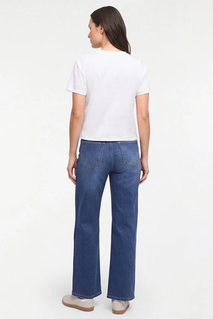 A woman shown from the back wearing a white short-sleeve t-shirt and blue straight-leg jeans, standing against a plain white studio background. 