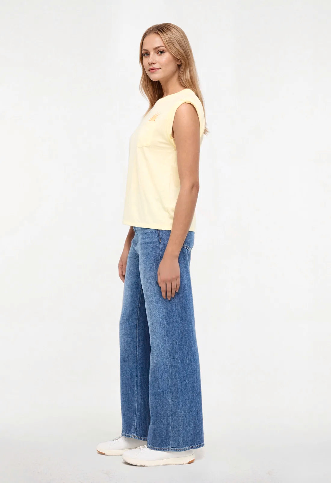 Side view of woman wearing a yellow sleeveless shirt with a sun and wave design and &