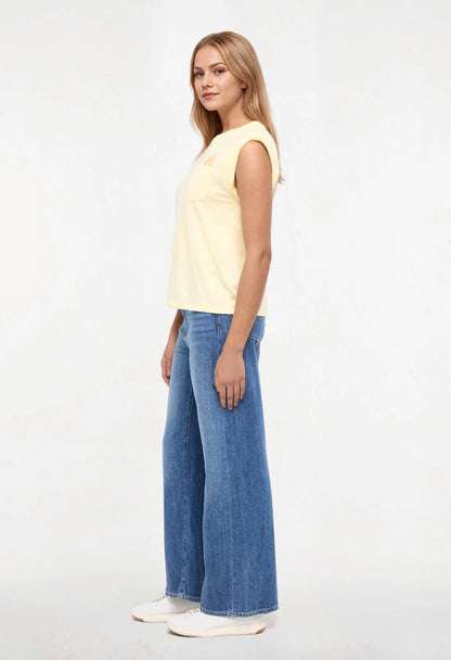 Side view of woman wearing a yellow sleeveless shirt with a sun and wave design and &