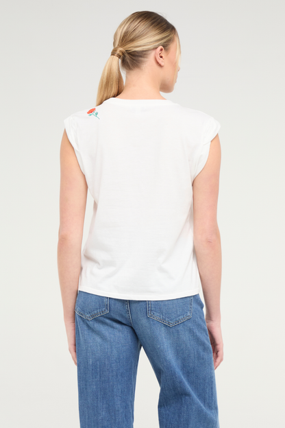 Back view of woman wearing white t-shirt with floral embroidery graphic design on top left shoulder and blue jeans on a white background. 