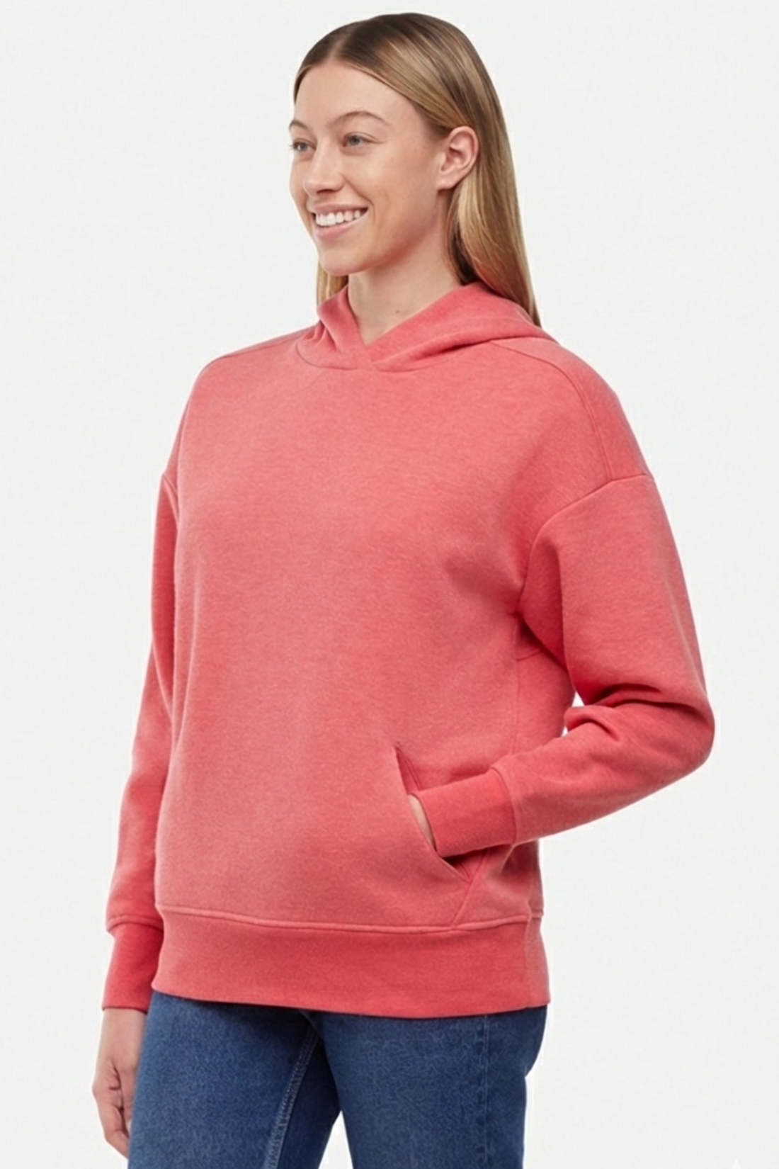 View of woman wearing a pink/red hoodie and blue jeans on a white background with hand in front kangaroo pocket.