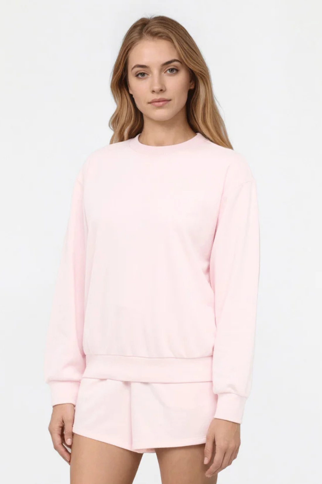 Front view of woman wearing a light pink sweatshirt and shorts set on a white background. 