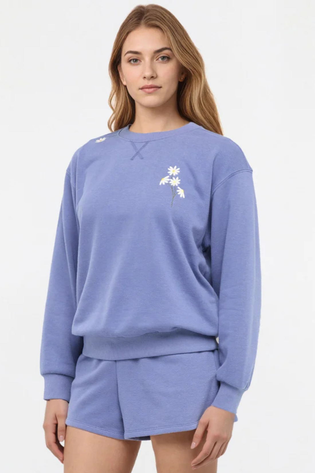 Front view of woman wearing a blue sweatshirt with floral designs on chest and shoulder and shorts on a white background. 
