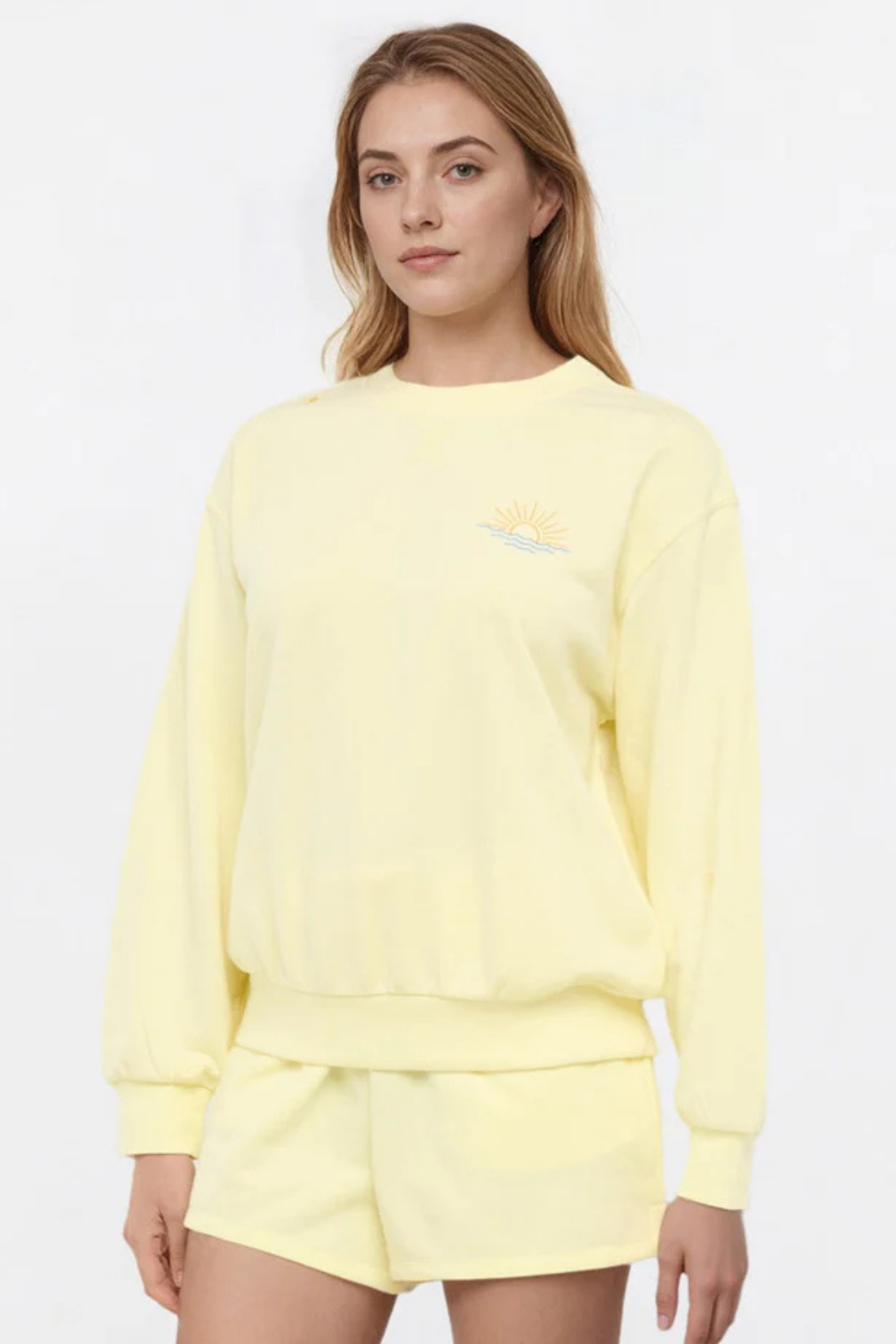 Front view of woman wearing a yellow sweatshirt and shorts on a light gray background. 