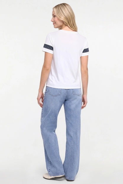 A woman is shown from the back wearing a white short-sleeve t-shirt with navy blue stripes on the sleeves and light blue wide-leg jeans, standing against a plain white studio background. 