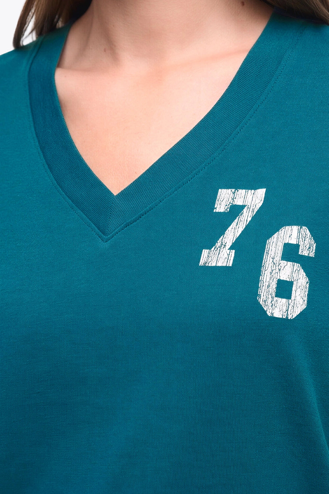 Close-up of a person wearing a teal V-neck t-shirt with a distressed white &