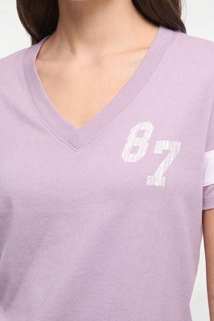 A close-up of a person wearing a light lavender purple V-neck t-shirt with a distressed white &