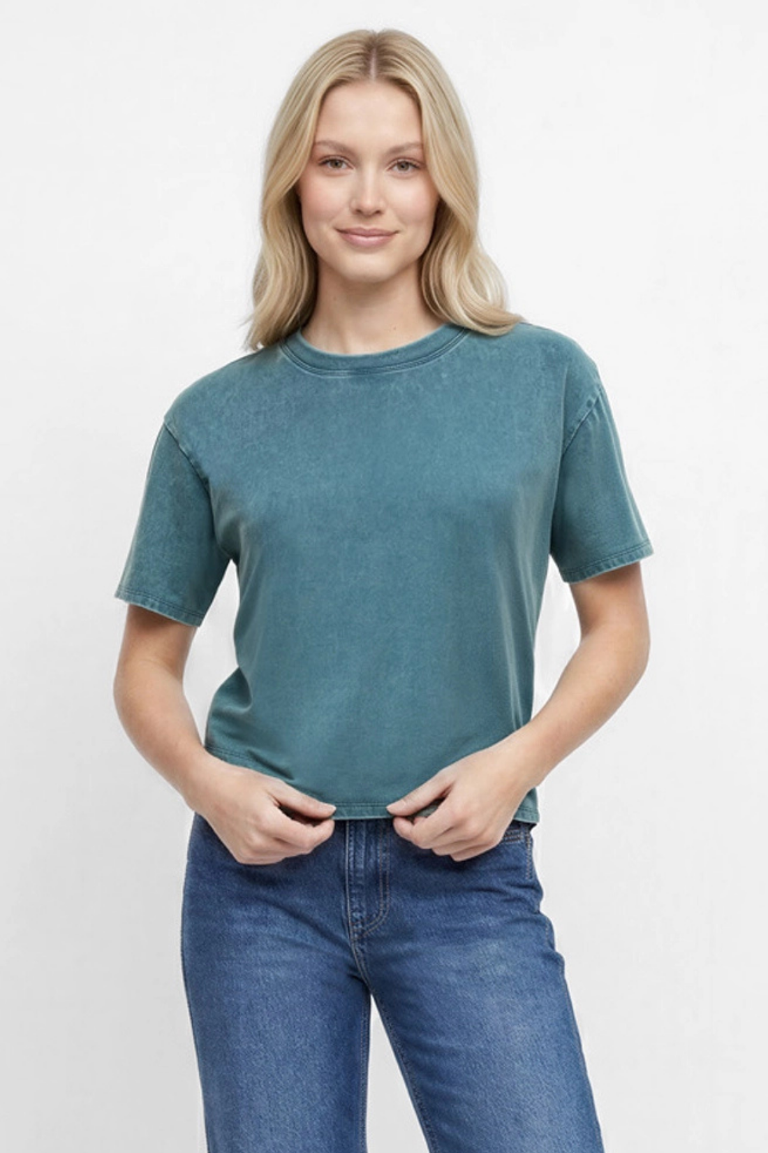 Front view of woman wearing a teal green t-shirt and blue jeans on a white background. 