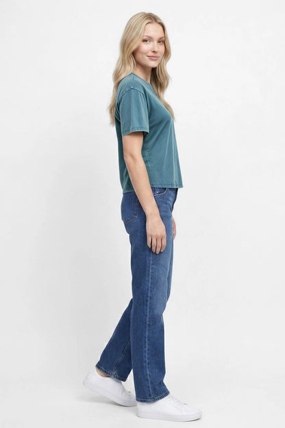 Side view of woman wearing a teal green t-shirt and blue jeans on a white background. 