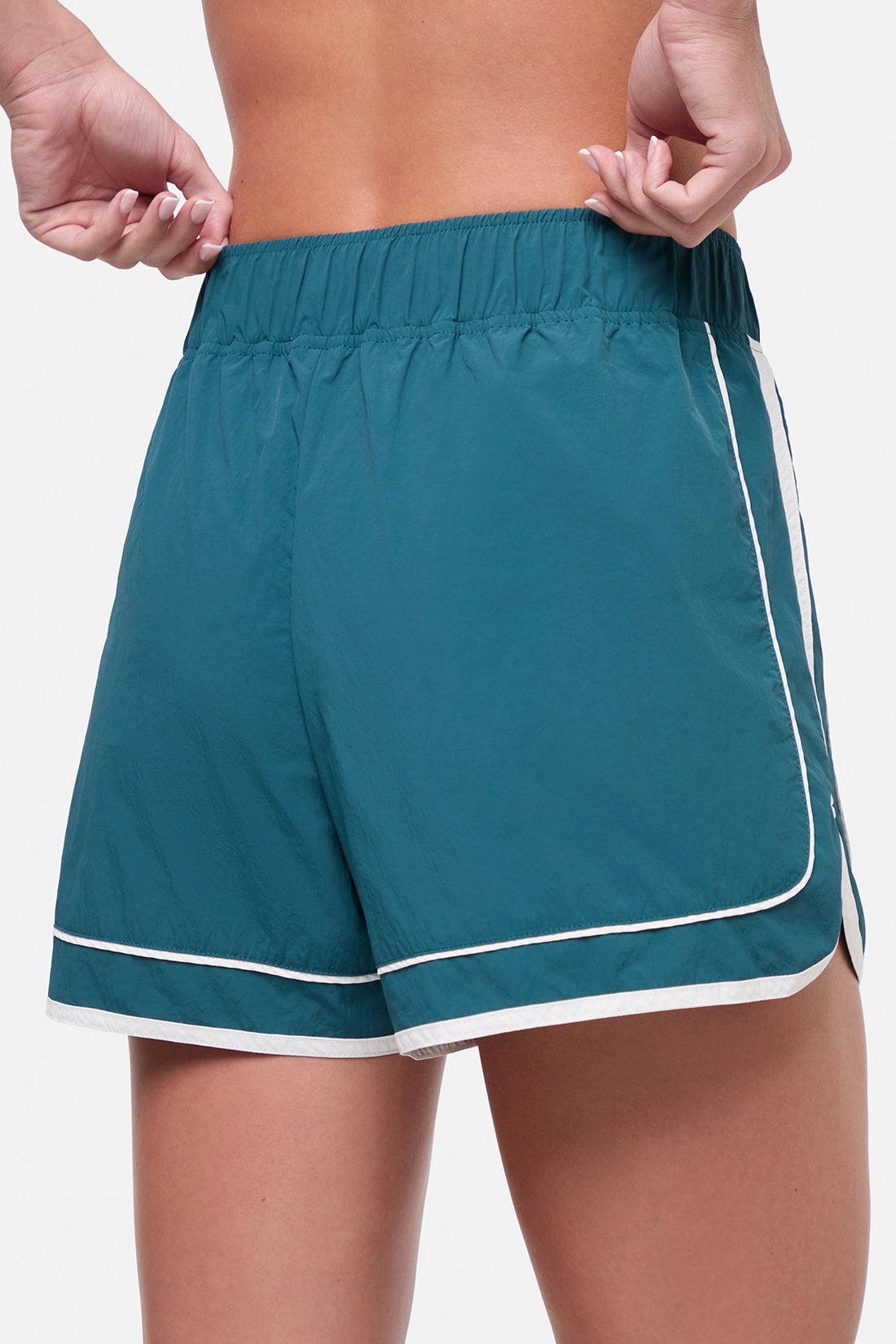 Close up back view of teal green athletic shorts with white trim worn by a woman on a white background. 