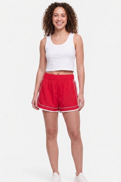 Front view of woman wearing a white tank top and red shorts on a white background. 