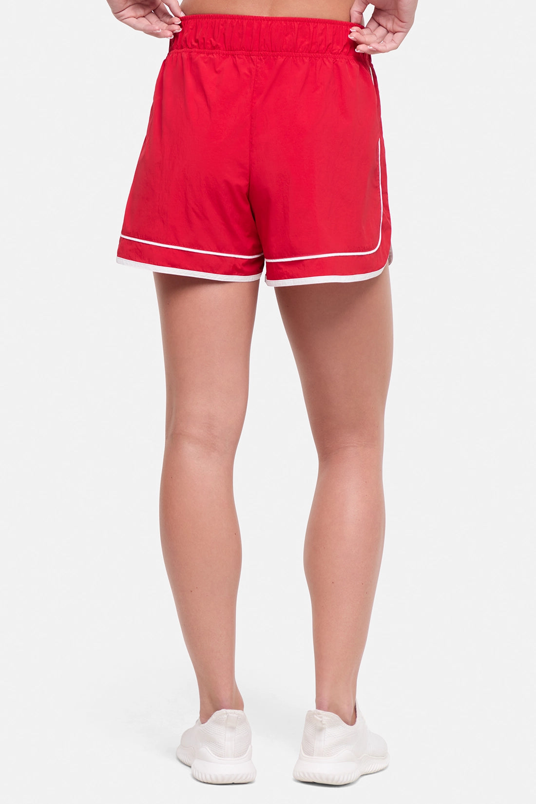 Back view of red athletic shorts with white trim worn by a woman on a white background. 