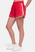 Side view of red athletic shorts with white trim worn by a woman on a white background. 