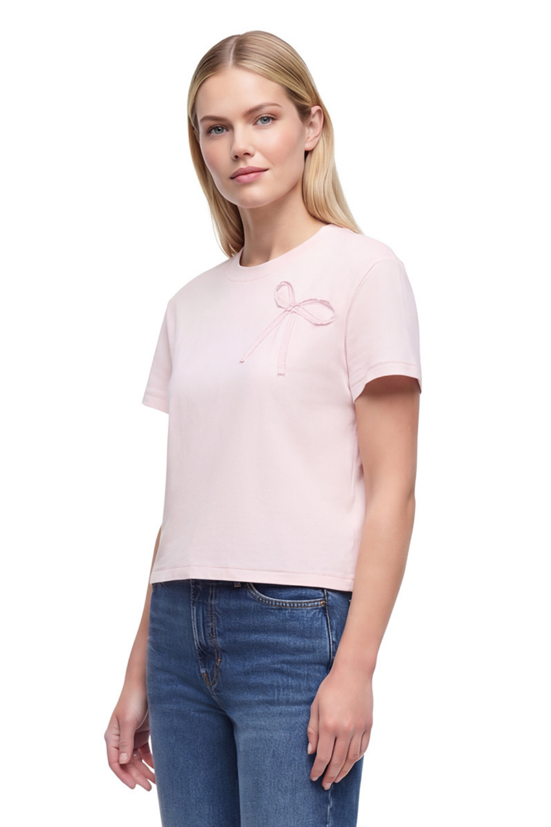 Front view of woman wearing a light pink t-shirt with a bow fabric design and blue jeans on a white background. 