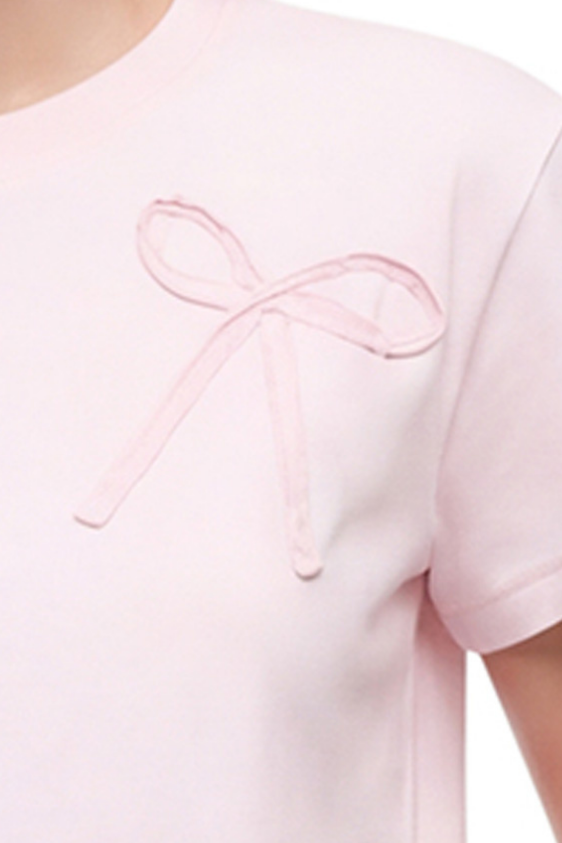 Close up view of view of woman wearing a light pink t-shirt with a bow fabric design and blue jeans on a white background. 
