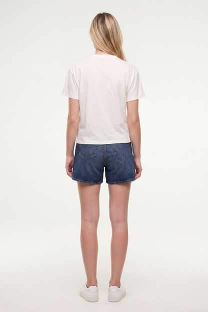 Back view of woman wearing a white t-shirt and jean shorts on a white background. 