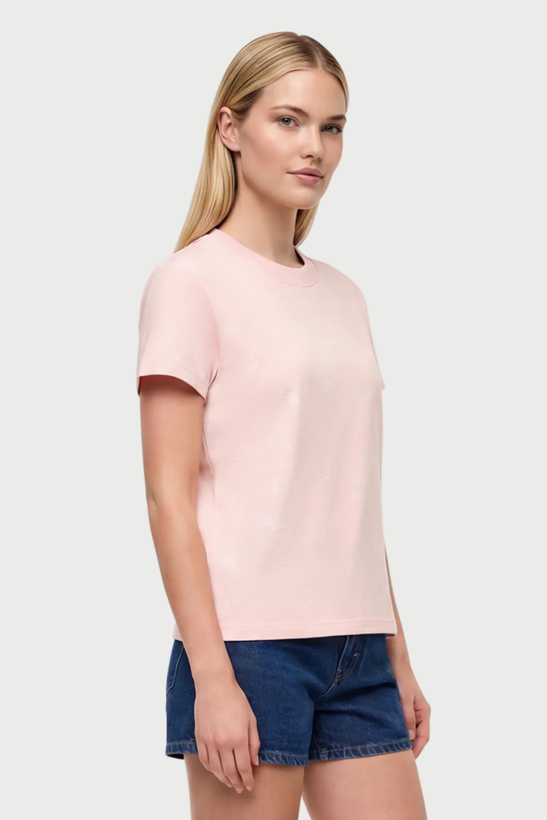 Front view of woman wearing a light pink t-shirt with pasta noodle shapes  pattern design and denim shorts on a white background. 