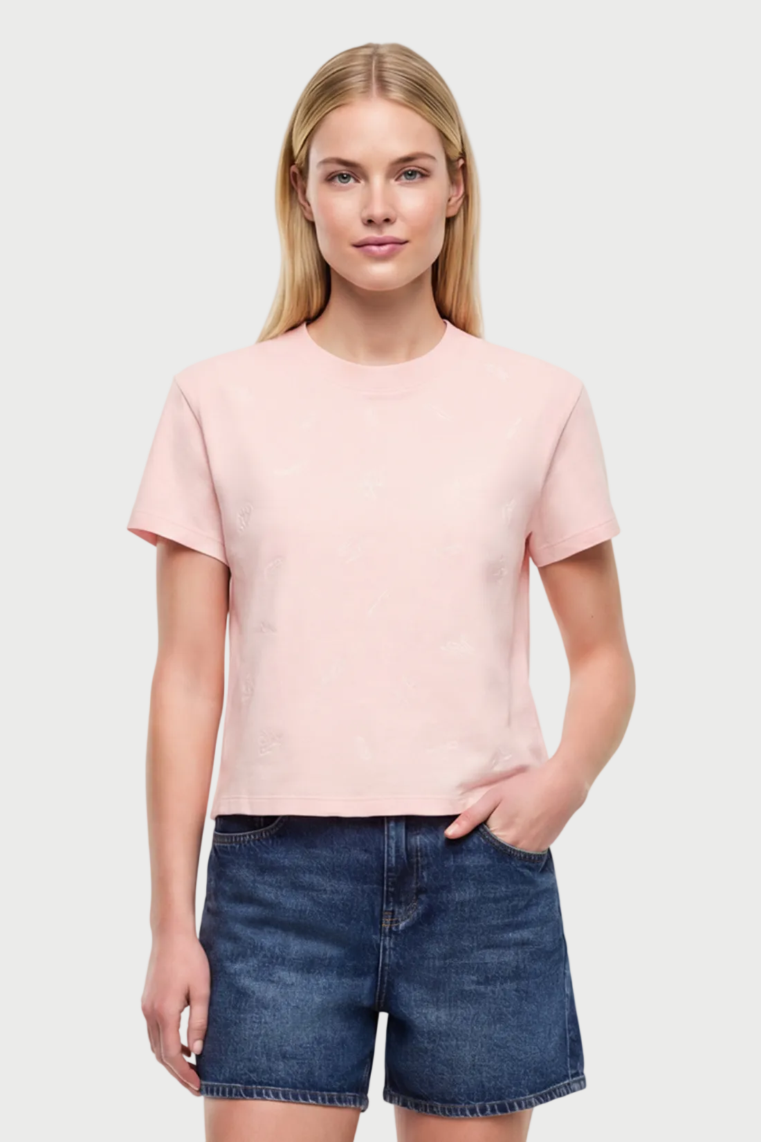Front view of woman wearing a light pink t-shirt with pasta noodle shapes  pattern design and denim shorts on a white background. 