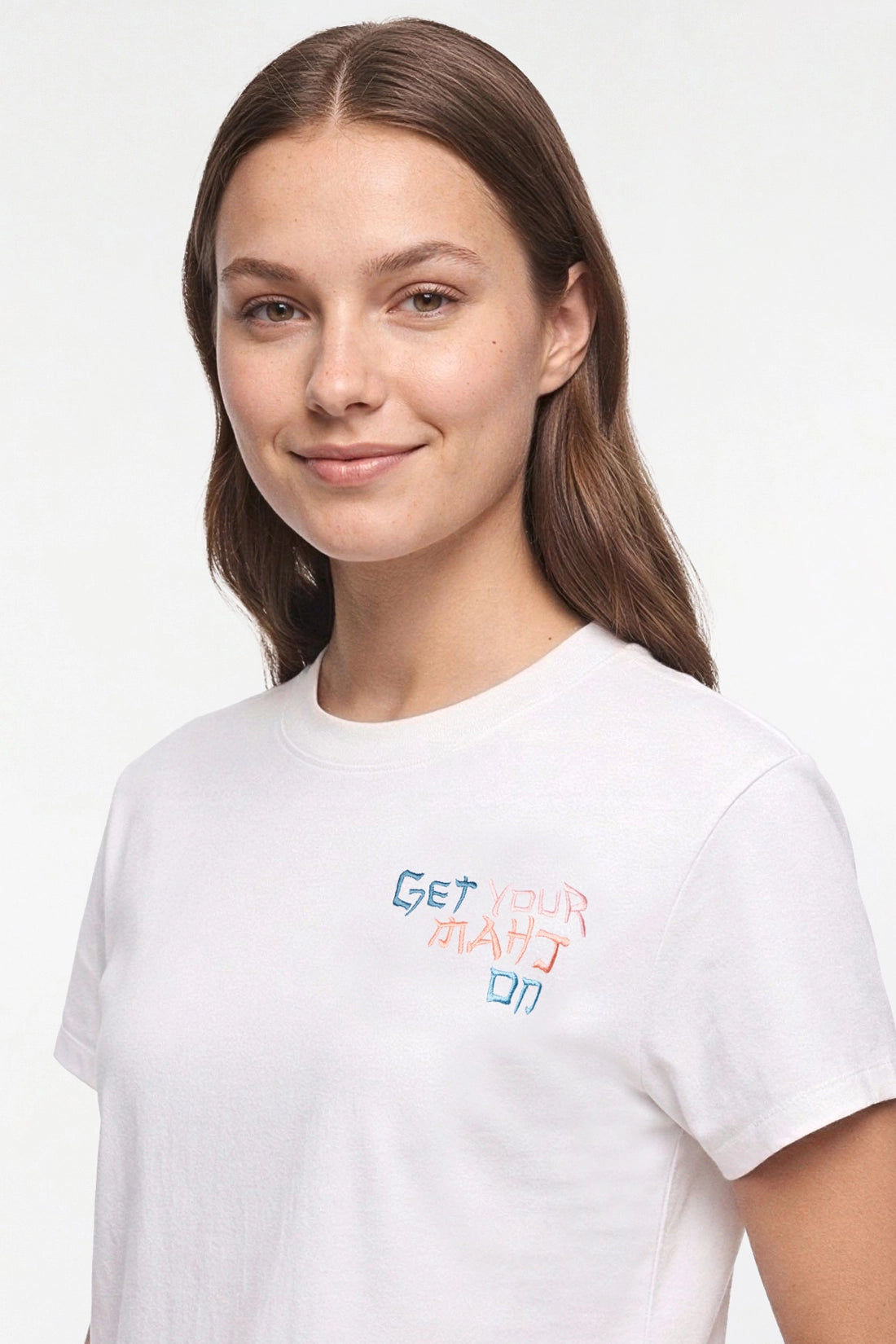 A woman wearing a white crew-neck t-shirt with a colorful graphic text print on the left chest that reads &