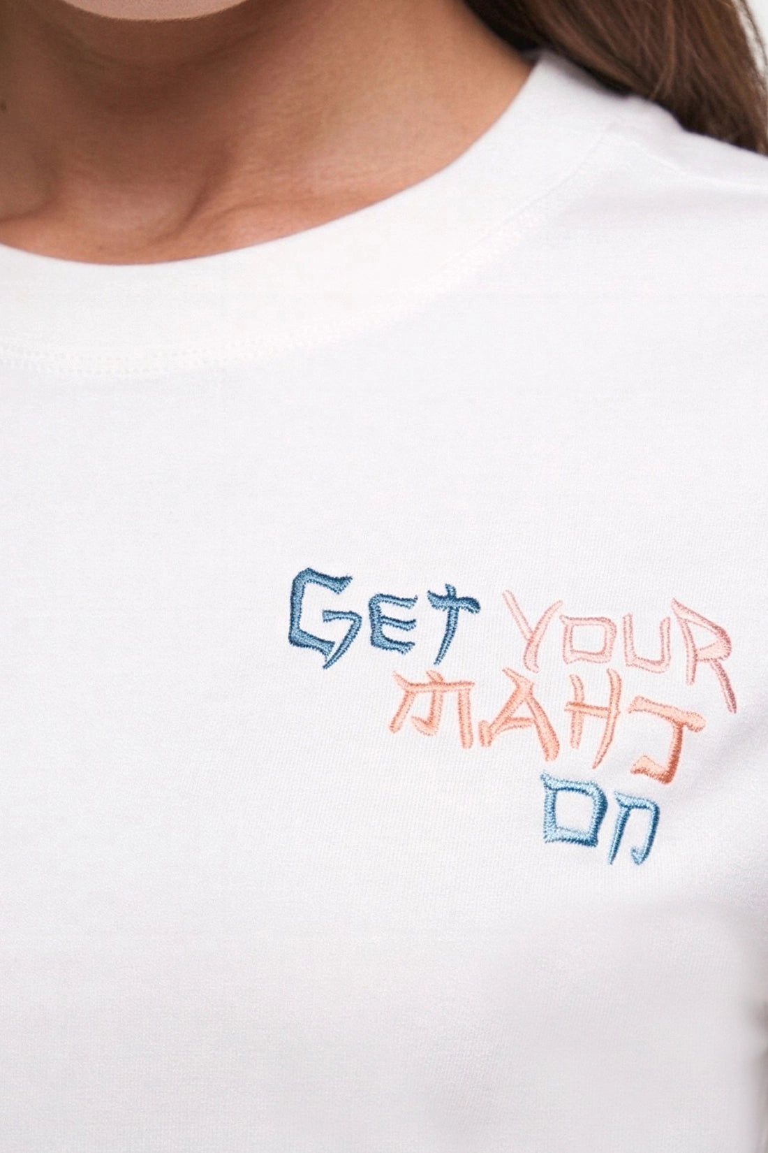 Close-up of a person wearing a white crewneck t-shirt with colorful embroidered text on the chest reading &