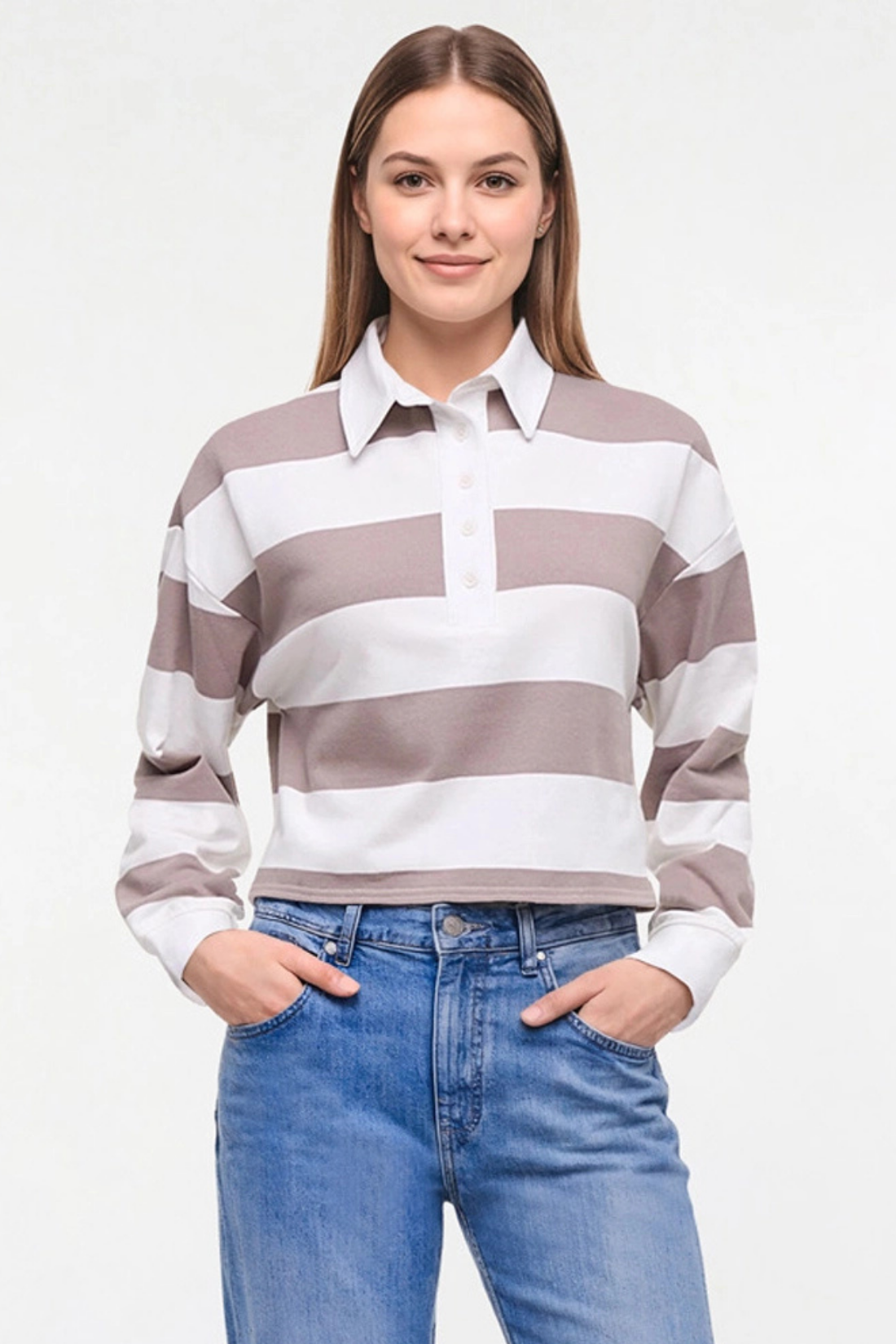 A woman modeling a long-sleeve collared knit Rugby polo top with horizontal taupe and white stripes, paired with blue jeans, against a plain white studio background. 