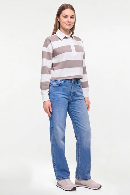 A woman modeling a long-sleeve collared knit top with horizontal taupe and white stripes, paired with blue jeans and light gray slip-on shoes, against a plain white studio background. 
