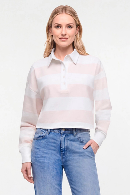 A woman modeling a long-sleeve knit polo shirt with horizontal white and pale pink stripes, paired with blue jeans, against a plain white studio background. 