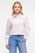 A woman modeling a long-sleeve knit polo shirt with horizontal white and pale pink stripes, paired with blue jeans, against a plain white studio background. 
