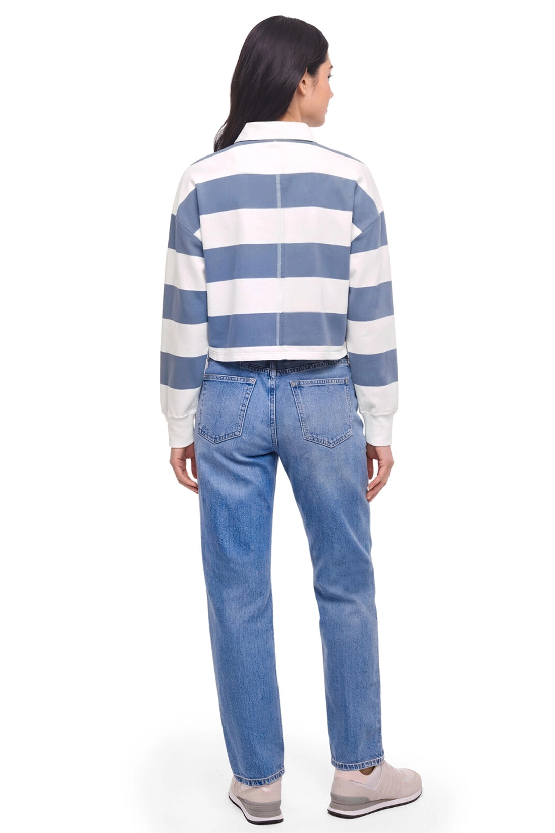 A model shown from the back wearing a blue and white horizontally striped cropped long-sleeve shirt and light blue jeans, against a plain white background. 