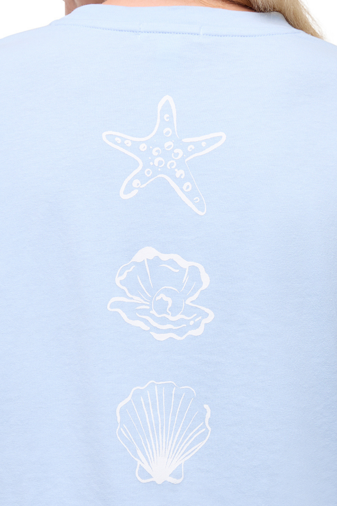 Close up view of light blue t-shirt with white starfish, shell, and pearl designs on a plain background. 