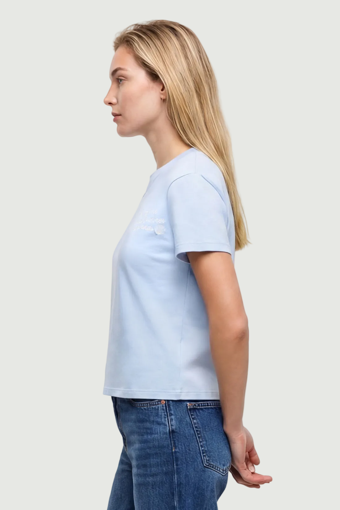 Side view of woman wearing light blue t-shirt with embroidered &