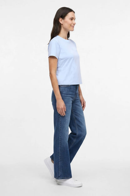 Side view of a woman wearing light blue t-shirt with embroidered &