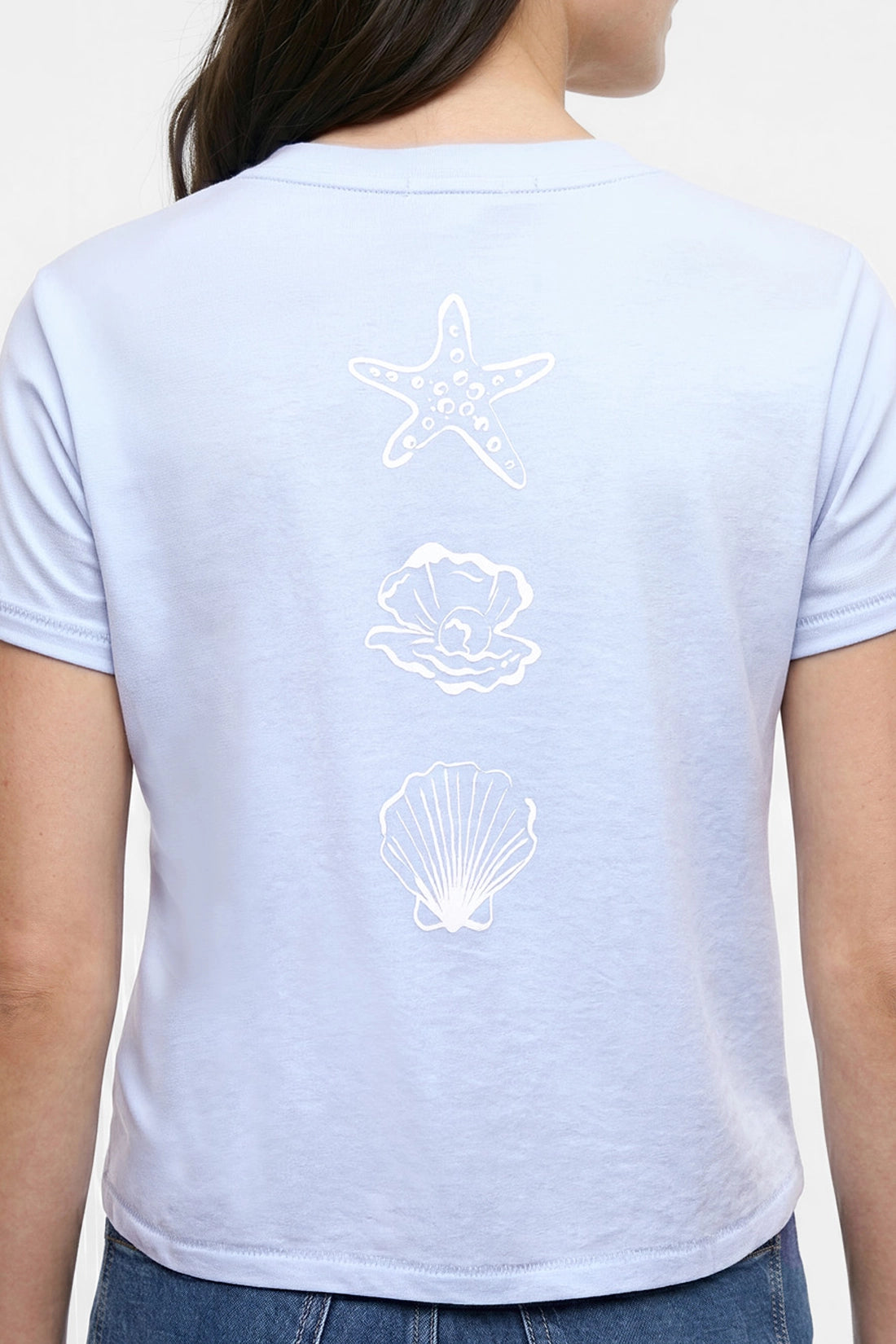 Back view of light blue t-shirt with white starfish, shell, and pearl designs on a plain background. 