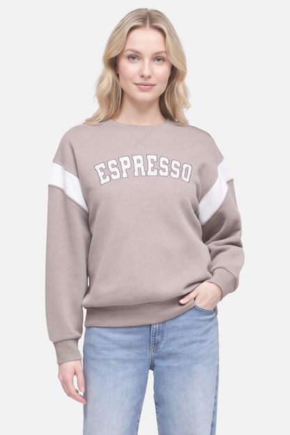 A woman wearing a taupe crewneck sweatshirt with white color-blocked sleeves and &