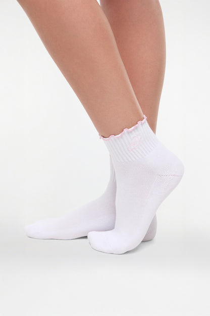 Side view of white socks with lilac ruffled trim and cheer megaphone graphic worn by a woman on a light background. 