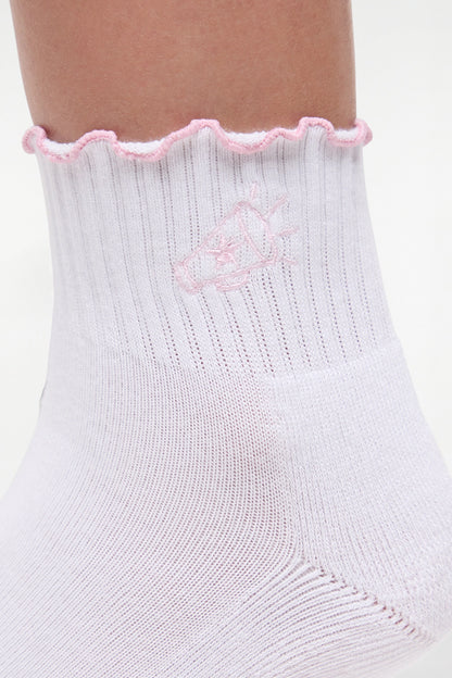 Close up view of white socks with lilac ruffled trim and cheer megaphone graphic worn by a woman on a light background. 