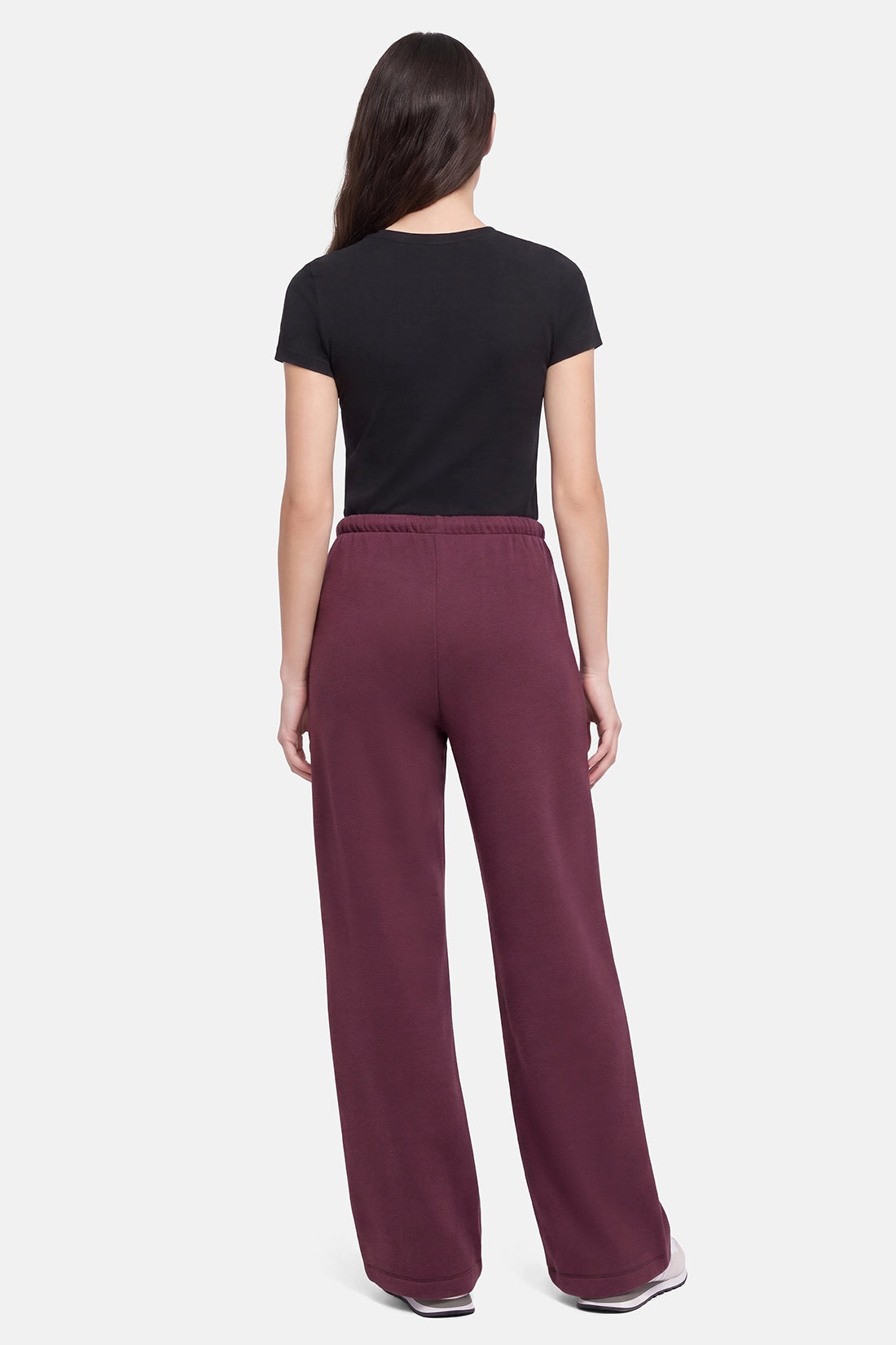 A woman shown from the back wearing a black short-sleeve t-shirt and wide-leg maroon sweatpants against a light gray studio background. 