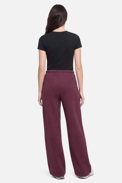 A woman shown from the back wearing a black short-sleeve t-shirt and wide-leg maroon sweatpants against a light gray studio background. 