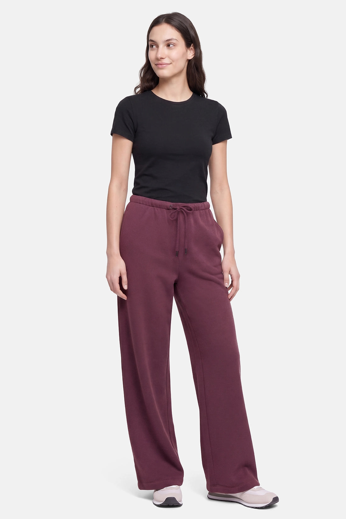A woman modeling a black short-sleeve t-shirt and burgundy wide-leg drawstring sweatpants against a light gray studio background. 